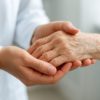 A close-up of a caregiver's hands gently holding an elderly person's hands, symbolizing support and care.